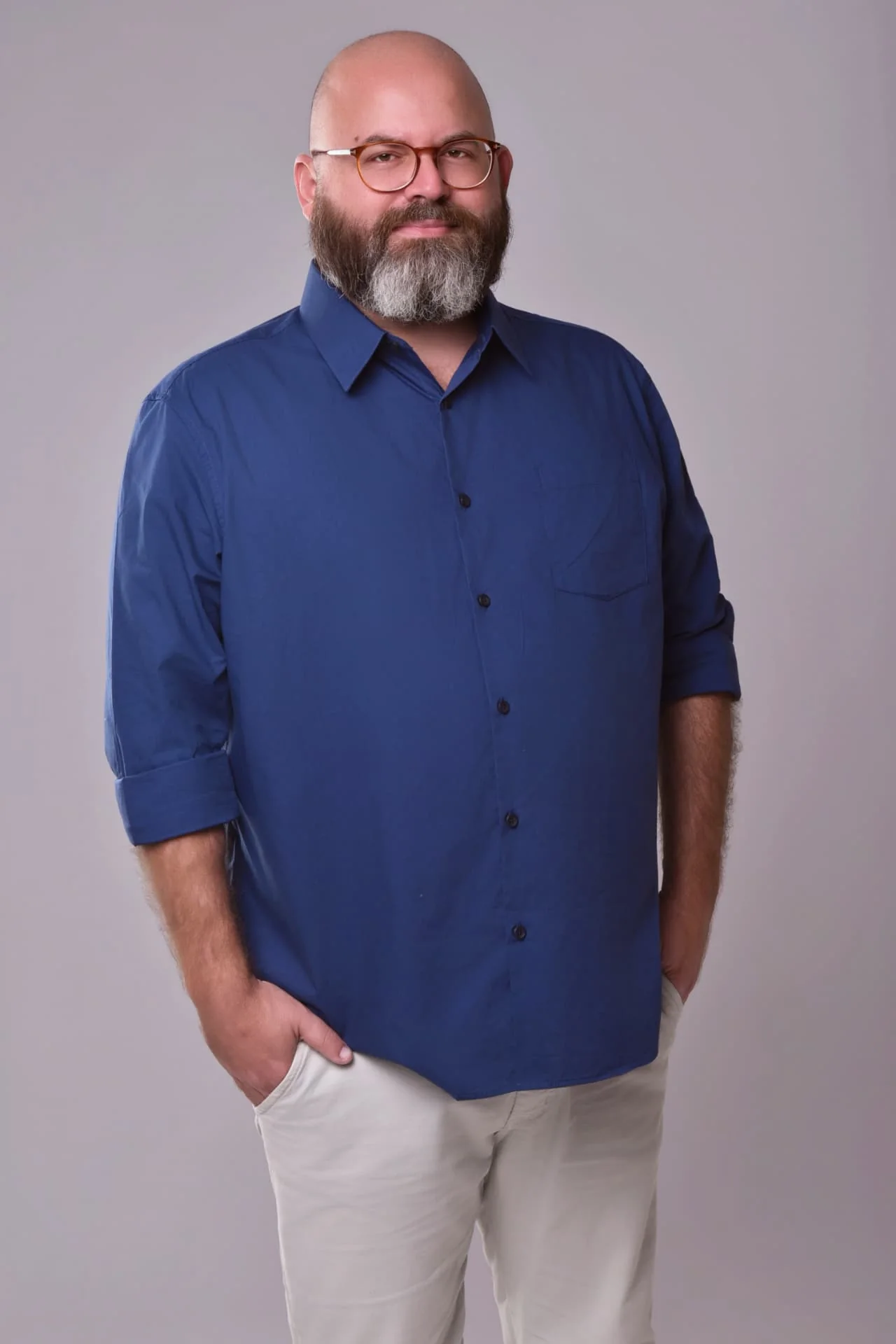 Carlos, de barba e óculos, com camisa azul, em retrato de estúdio